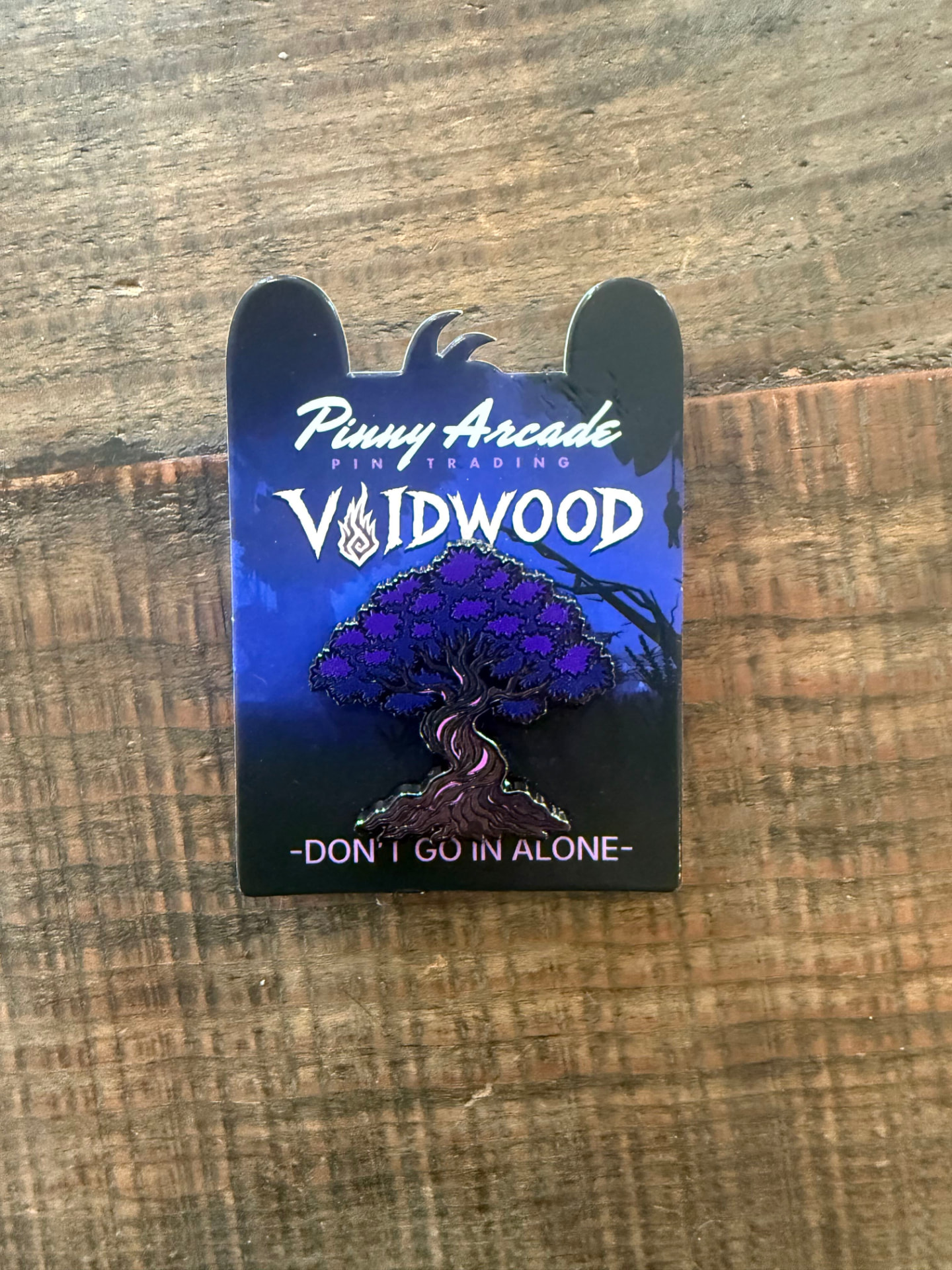 The Voidwood Pinny Arcade pin on its backer card, reading Don't Go In Alone